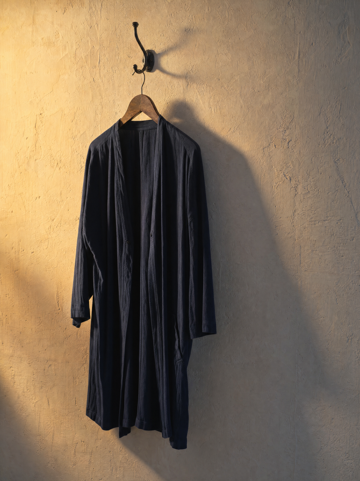 A coat hanging on a single hook in low raking sunlight