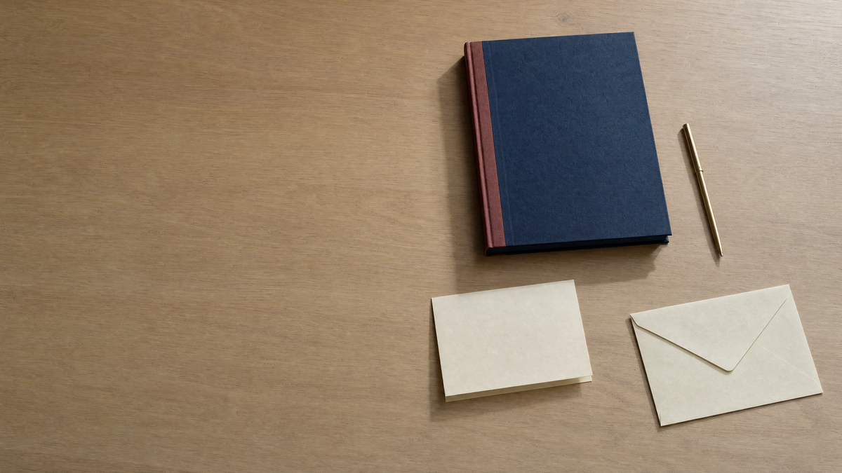A wooden desk seen from above with a red ledger, loose paper and a pen, open space on the left