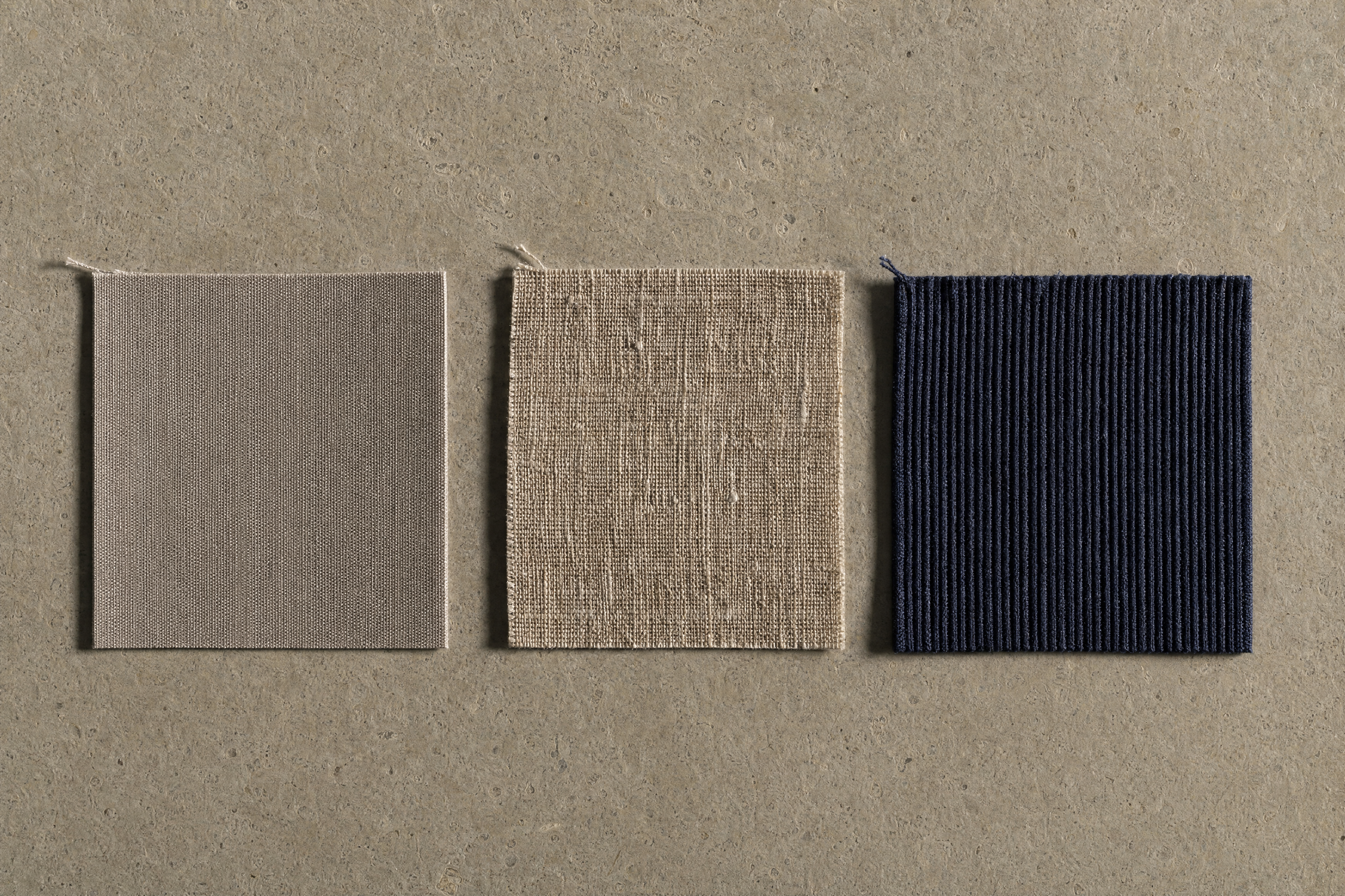 Three folded fabric swatches in muted tones stacked on a plain surface